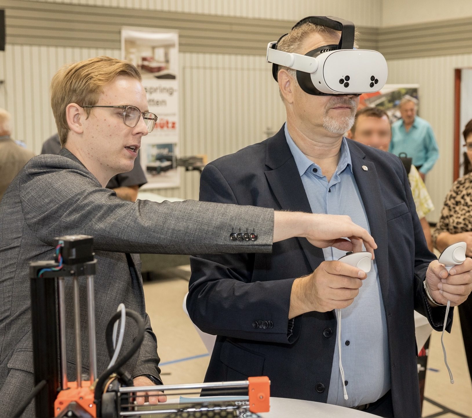 Robert Fischbach explaining a VR headset to a participant, with a 3D printer in the foreground